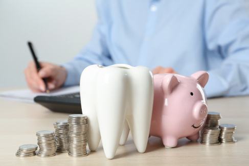 A ceramic model of a tooth, a piggy bank, and coins on a wooden table