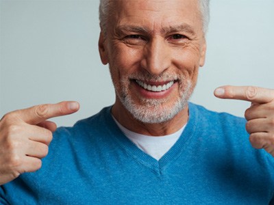 A happy and smiling senior man pointing out his new dentures