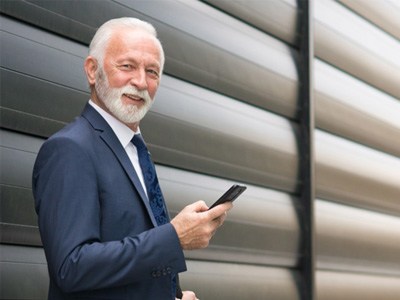 A senior businessman using his phone in front of a corporate office building