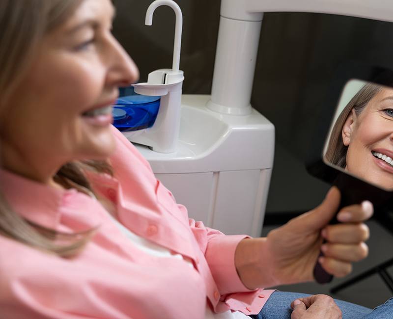 Middle-aged dental patient admiring her smile in the mirror