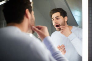 Man looking in mirror and pulling back lip to inspect his dental implant